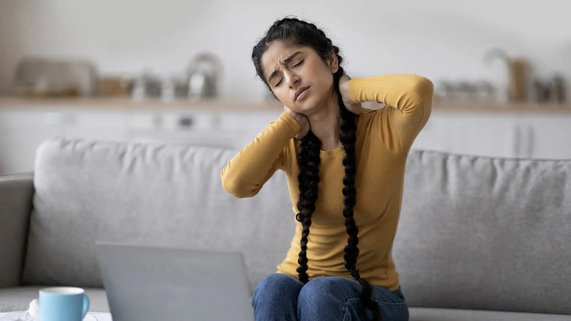 Woman experiencing neck pain while sitting on couch