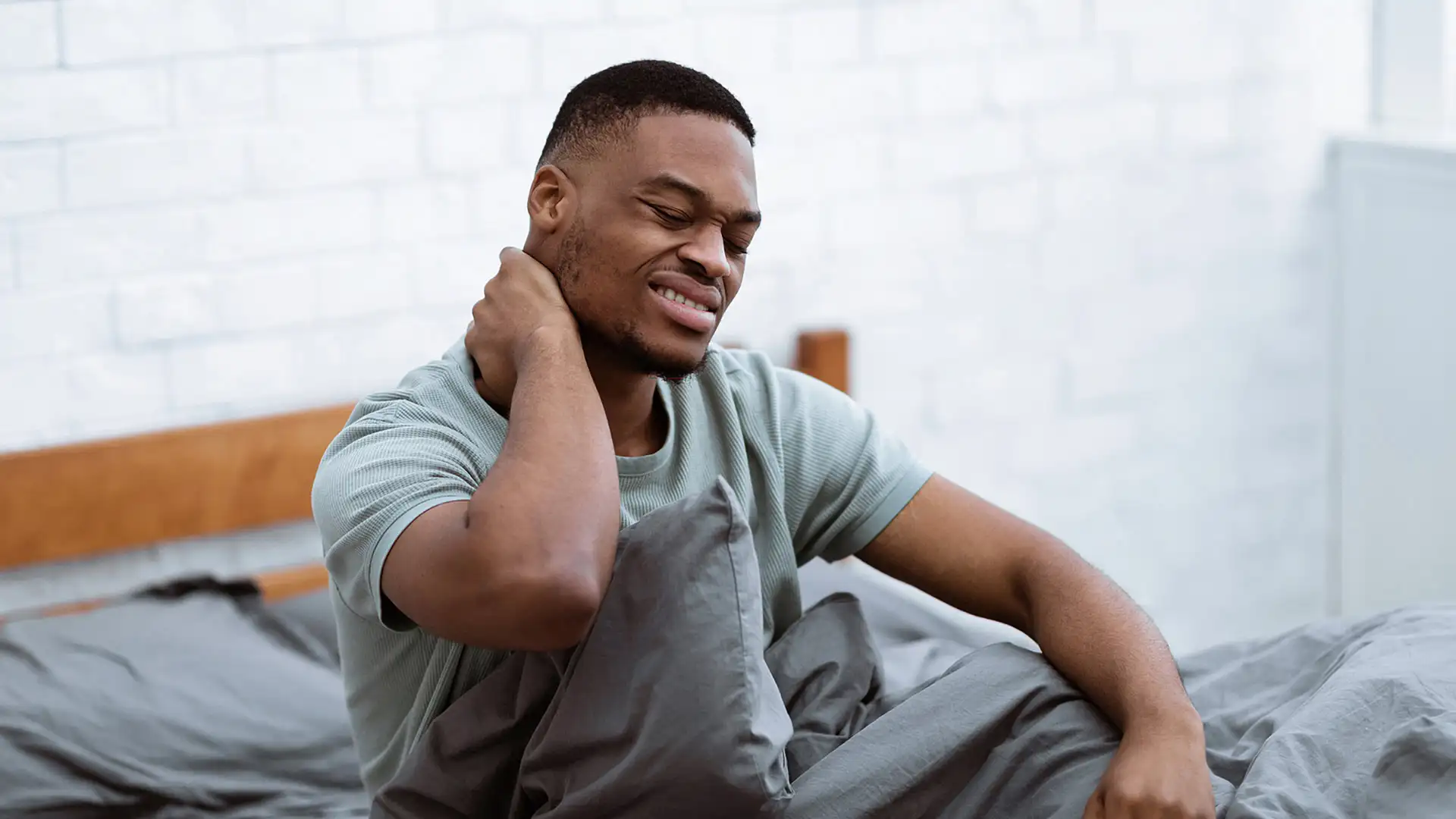 A man suffering from Neck Pain waking up in bed