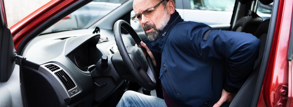 Man touching lower back in pain, while sitting in car.